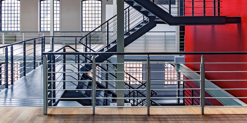 An Image of staircase span of the wall of red color with metal railings and wooden floor tiles.